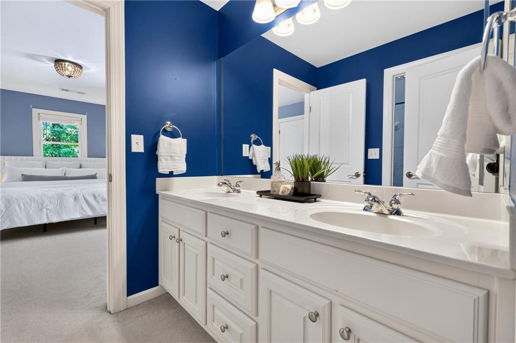 Bathroom with a white double-sink vanity, blue walls, and a view into the adjoining bedroom.