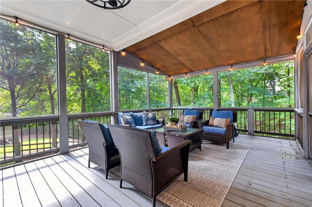 Screened porch with wicker seating, a patterned rug, string lights, and leafy wooded views.