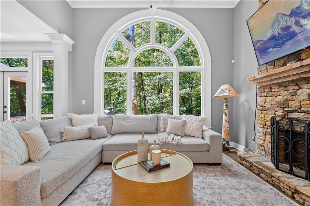 Living room with a tall arched window overlooking trees and a stone fireplace beside a light sectional sofa.