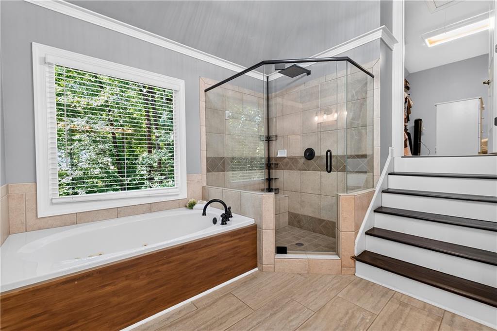 Bathroom with a wood-paneled tub, glass shower, and stairs beside a window overlooking trees.