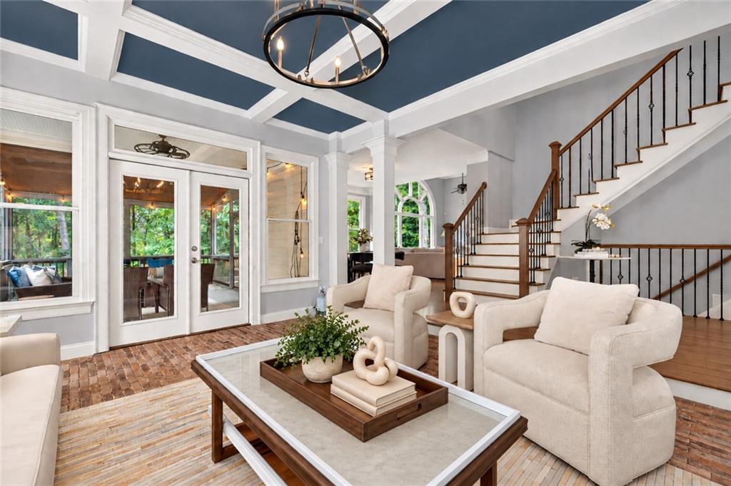 Living room with a blue coffered ceiling, white seating, brick flooring, and a staircase.