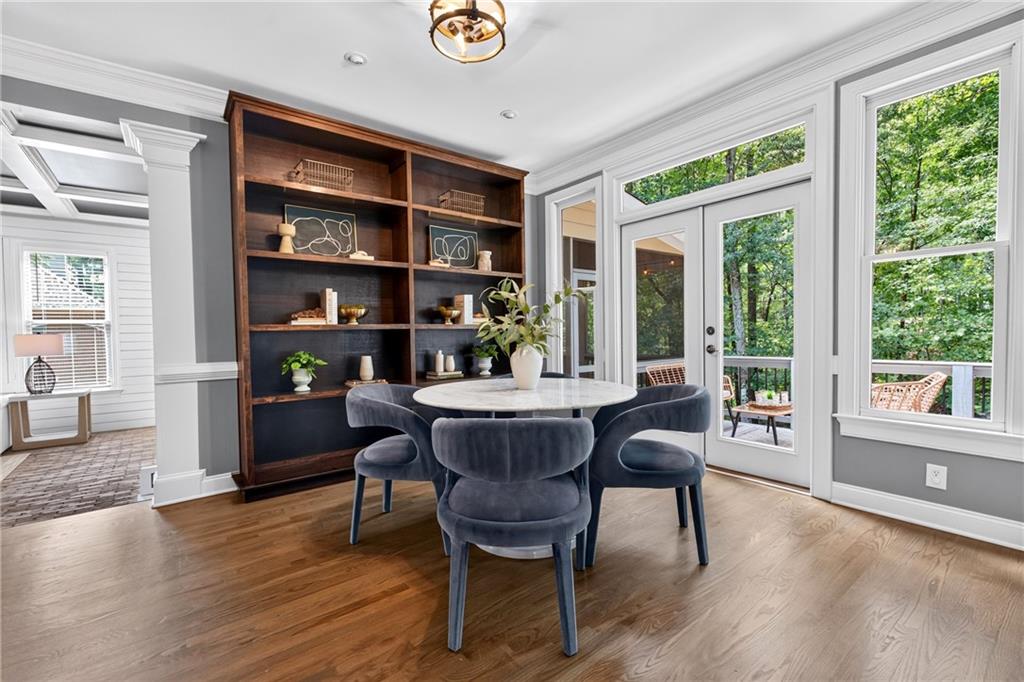 Dining area with built-in shelving, a round table, hardwood floors, and windows overlooking a wooded deck.