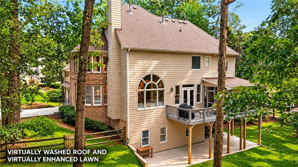 Rear of a beige-sided home with a raised deck and arched window among mature trees.