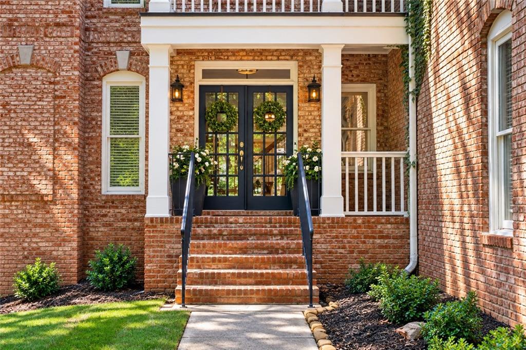 Brick home entrance with wreath-adorned double doors, covered porch, and brick steps.