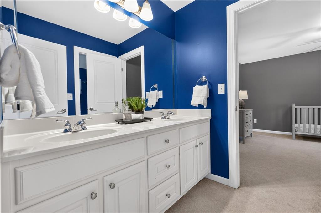 Bathroom with a long white double-sink vanity and vivid blue walls, opening onto a room with a crib.