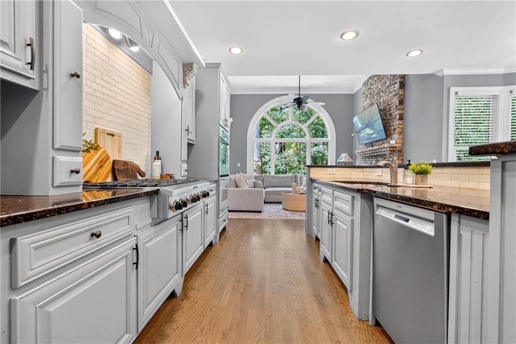 Kitchen with white cabinets and dark counters, opening to a living room with a large arched window.