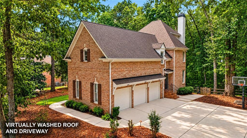 Two-story brick house with a three-car garage and broad driveway, surrounded by mature trees.