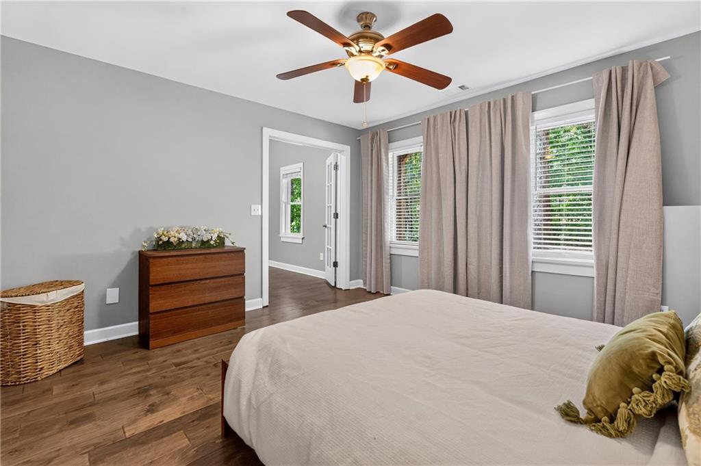 Bedroom with a large bed, ceiling fan, wood-look floors, and curtained windows.