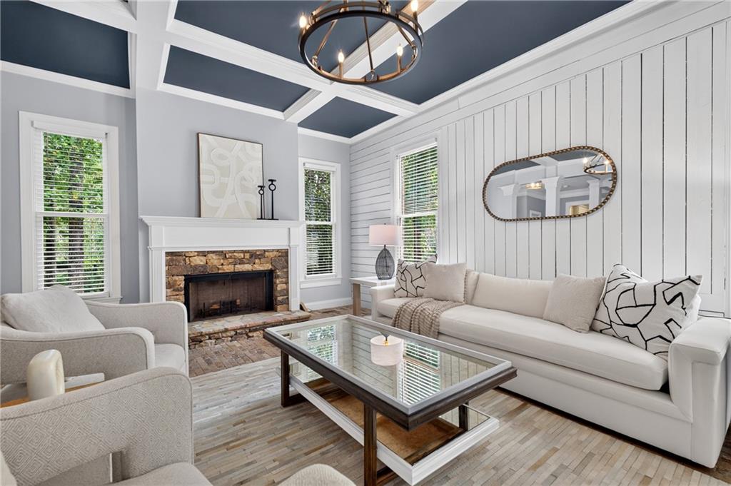 Staged living room with a stone fireplace, white sofas, glass coffee table, and coffered ceiling.