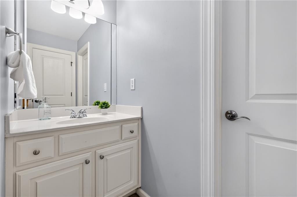 Bathroom vanity with white paneled cabinets, a large mirror, and a small potted plant.