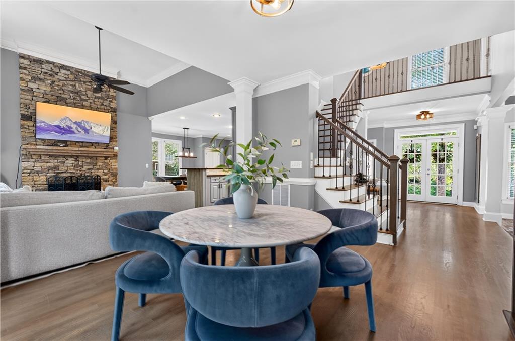 Open-plan dining and living area with a stone fireplace, blue dining chairs, and a staircase.