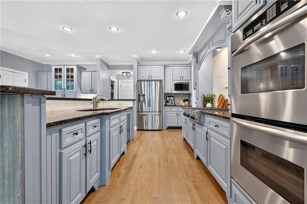 Kitchen with blue-gray cabinets, dark countertops, stainless steel appliances, and warm wood flooring.