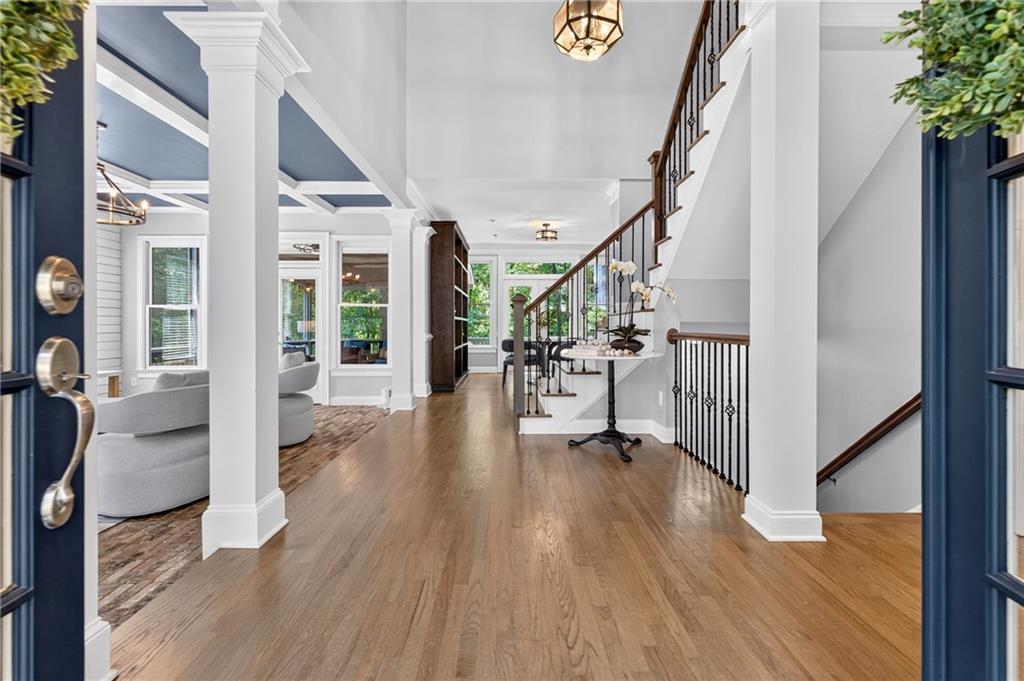 Home foyer with hardwood floors, white columns, a staircase, and a furnished sitting area.