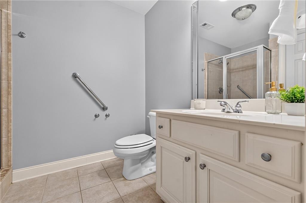 Bathroom with a white vanity, toilet, tiled floor, and glass-enclosed shower.