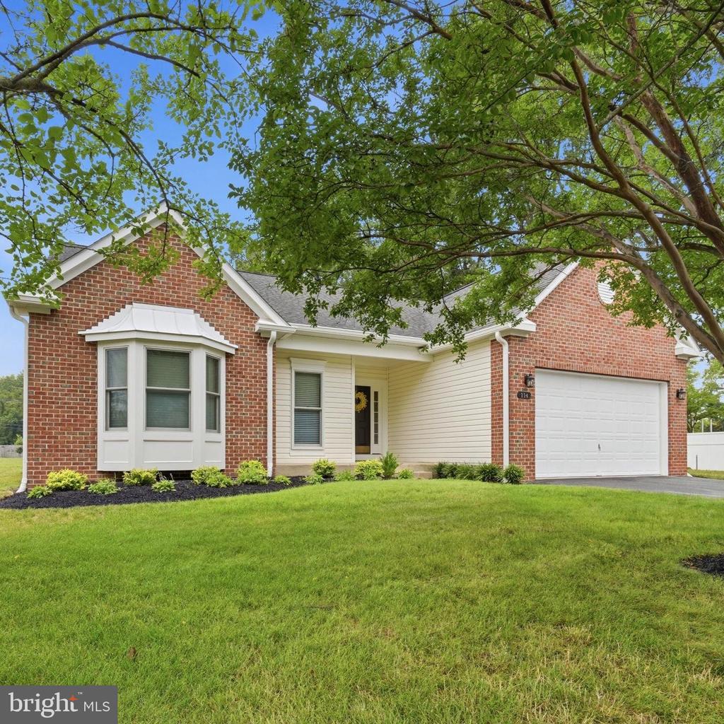 Single-story brick house with a white bay window, two-car garage, and leafy tree over the lawn.
