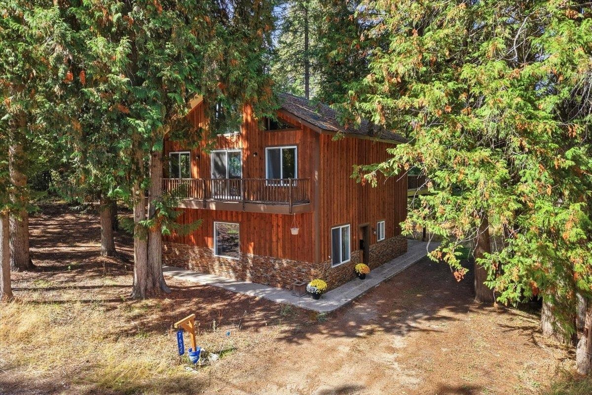 Wood-sided two-story home with a balcony nestled among tall evergreen trees.