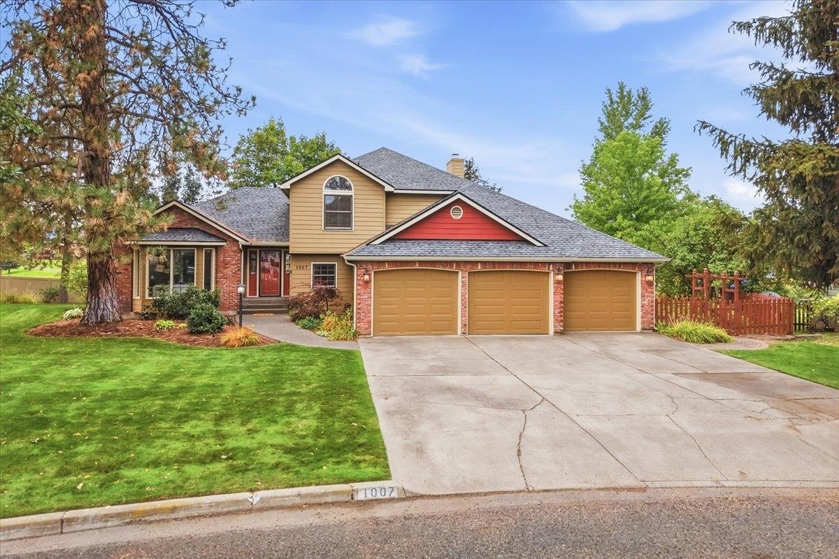 Two-story tan and brick home with red accents, a three-car garage, and a broad driveway.