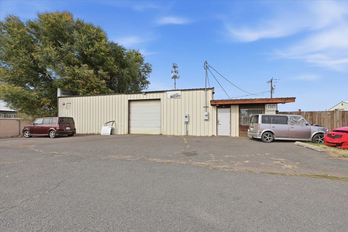 Commercial building with a roll-up garage door and attached office, fronted by a broad paved parking area.