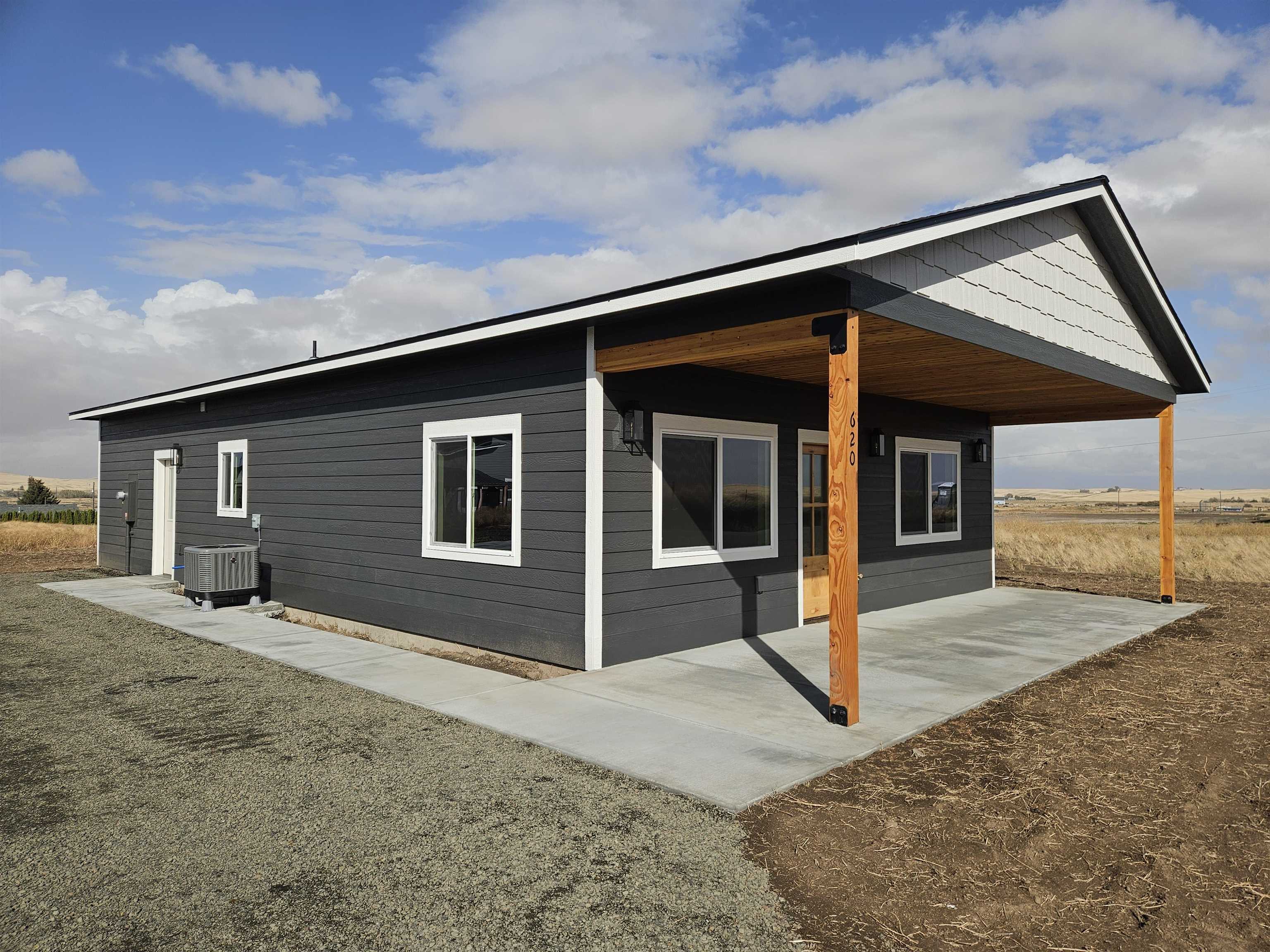Modern dark gray house with white trim and a broad covered patio on timber posts.