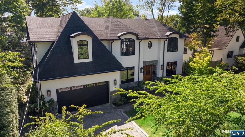 Two-story white house with dark gables, a stone entry, and a paved driveway amid mature trees.