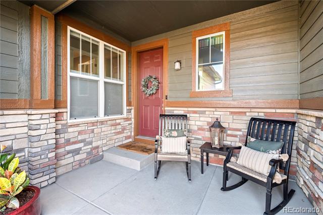 Covered front porch with a red door, stone veneer, and two cushioned rocking chairs.