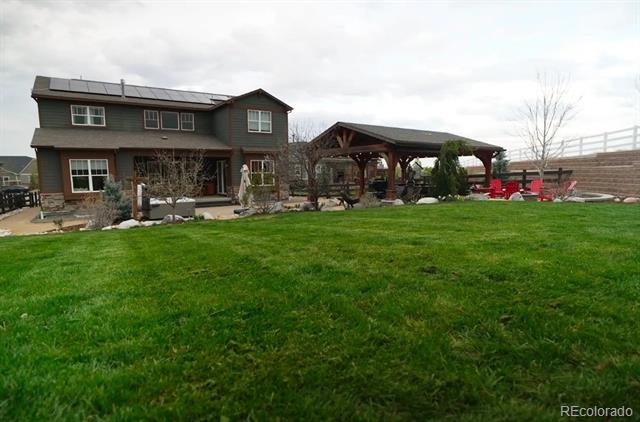 Rear of a two-story home with solar panels, a covered patio pavilion, and a broad green lawn.