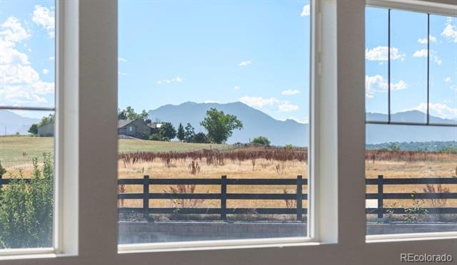 Mountain range and open field viewed through large windows above a dark wooden fence.