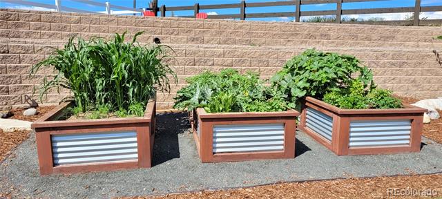 Three raised wooden garden planters with metal fronts sit on gravel beside a block retaining wall.