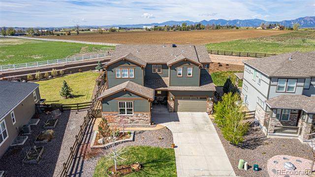 Two-story green house with stone accents and a concrete driveway, photographed from above with mountains in the distance.