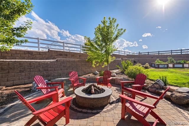Stone patio with a circular fire pit and red Adirondack chairs beside a lawn.