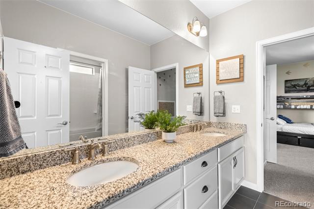 Bathroom with a long granite double vanity, white cabinetry, and a potted plant.