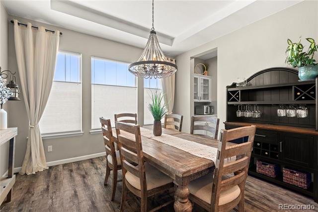 Dining room with a rustic wood table, chandelier, tall curtained windows, and dark built-in hutch.