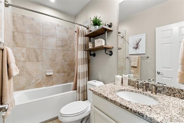 Bathroom with tiled tub and shower, granite vanity, and white cabinetry.