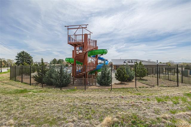Fenced playground with a tall wooden climbing tower and green and blue slides.