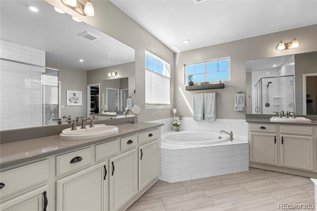 Bathroom with a long vanity, soaking tub beneath two windows, and glass-enclosed shower.