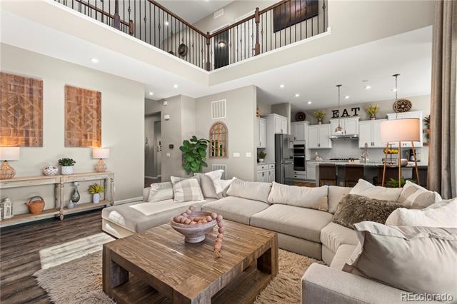 Double-height living room with a large sectional, wood coffee table, and open kitchen.