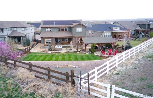 Two-story home with a covered patio, landscaped backyard, and white and wooden fences.