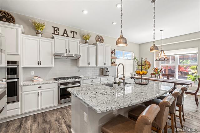 Bright kitchen with white cabinets, a granite island, pendant lights, and bar seating.