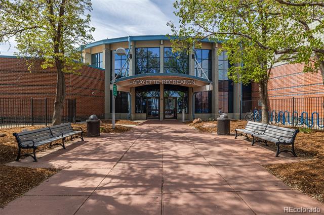 Lafayette Recreation entrance with a glass facade, brick walls, benches, and leafy trees.