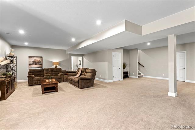 Lower-level living room with brown sofas, beige carpet, recessed lights, and an open layout.
