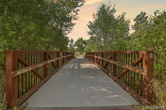 Concrete walking bridge with rust-colored railings crossing a tree-lined path.
