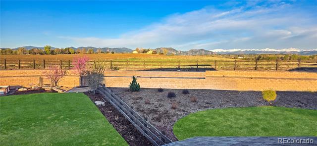 Backyard with green lawns, landscaped beds, a fenced field, and mountain views.