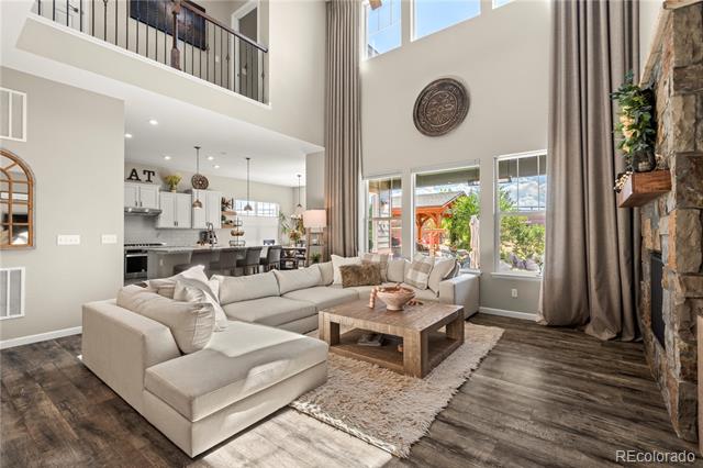 Double-height living room with a beige sectional, stone fireplace, and open kitchen.