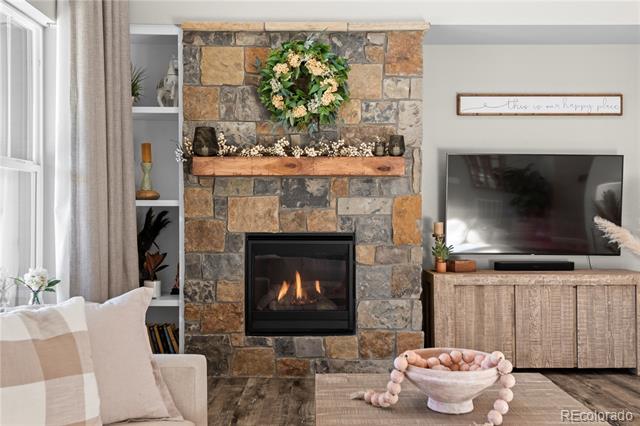 Living room with a stone fireplace, lit fire, wreath, and television.