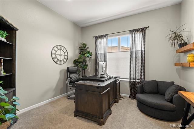 Home office with a dark wooden desk, curved sofa, and window with patterned curtains.