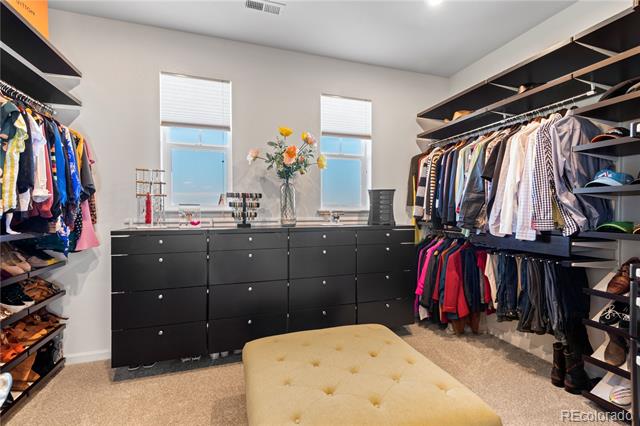 Walk-in closet with black drawers, clothing-lined shelves, two windows, and a cream tufted ottoman.