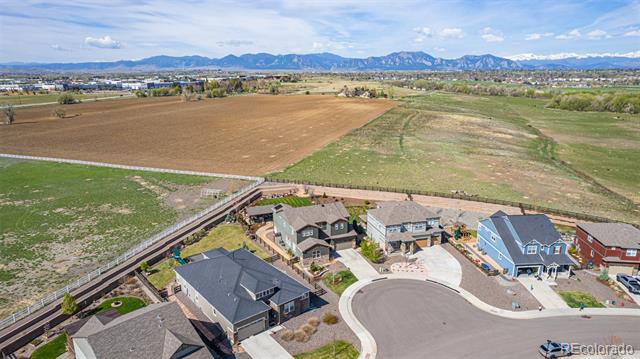 Aerial view of homes beside open farmland, with the Rocky Mountains in the distance.