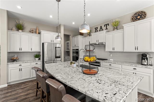 Kitchen with white cabinetry, stainless appliances, and a large stone island with bar stools.