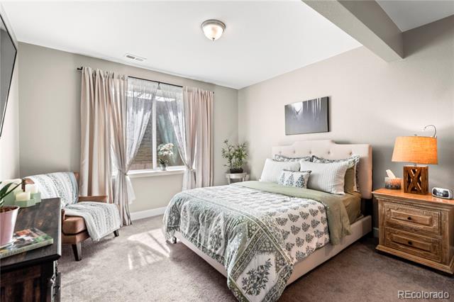 Bedroom with patterned bedding, a pale upholstered headboard, and a window with sheer curtains.