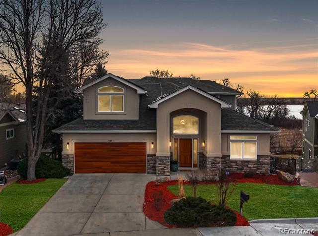 Two-story gray home with a wooden garage door and water visible behind it at dusk.